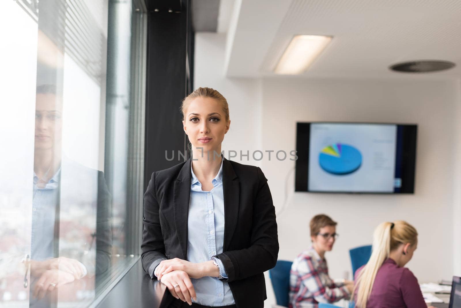 portrait of young business woman at office with team on meeting in background by dotshock