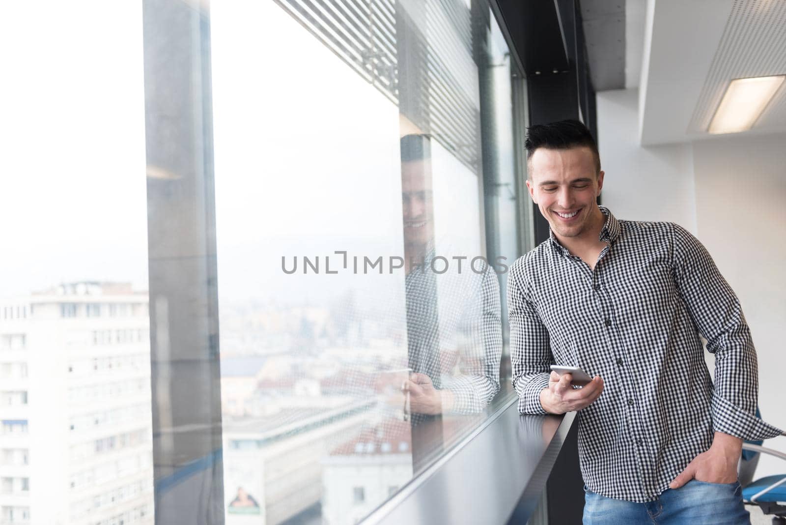 relaxed young businessman using smart phone at modern startup business office meeting room  with big window and city in backgronud