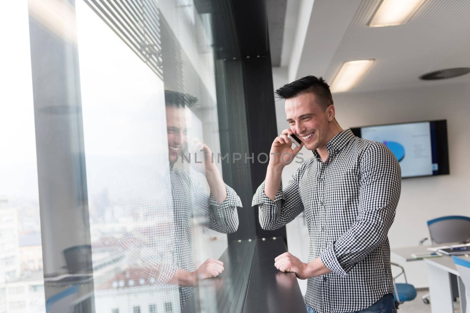 relaxed young businessman speaking on smart phone at modern startup business office meeting room  with big window and city in backgronud