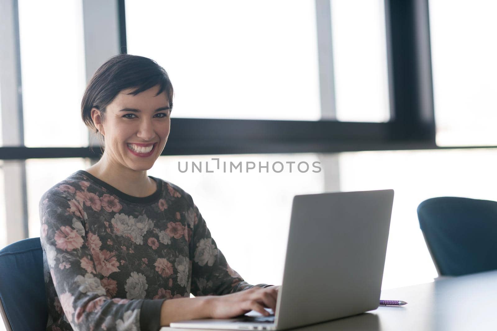 young  business woman at modern startup office interior working on laptop computer, blured team in meeting, people group in background