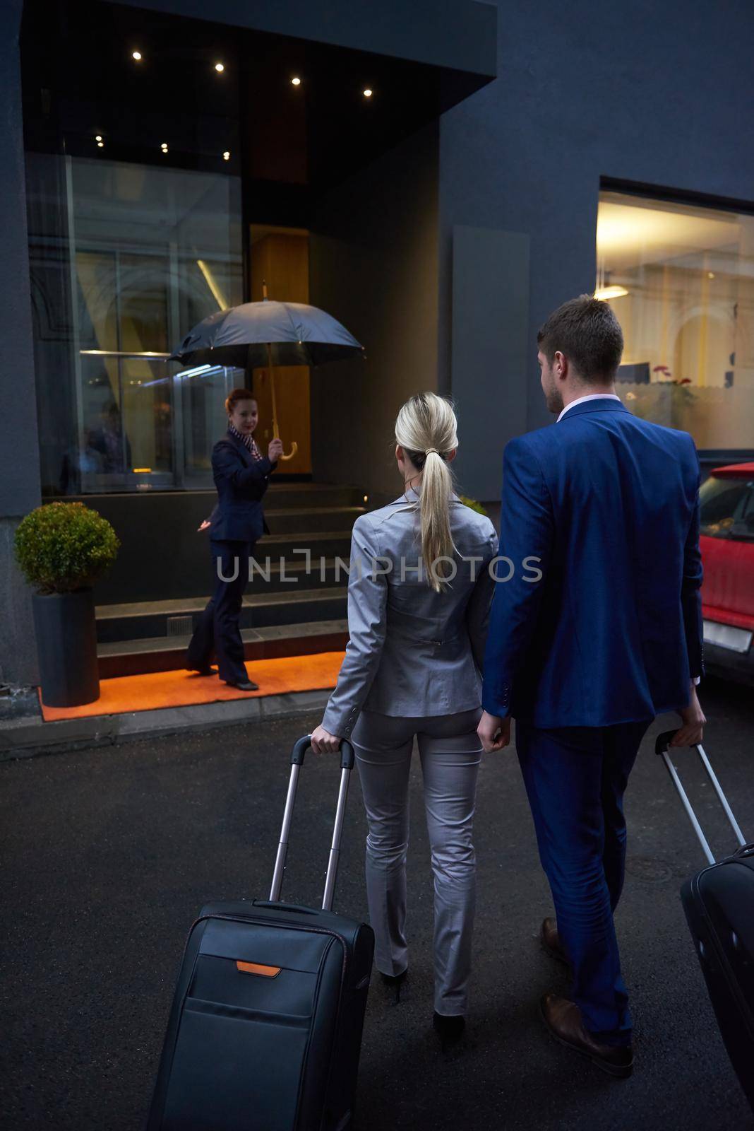 Young business people couple entering city  hotel, looking for room, holding suitcases while walking on street