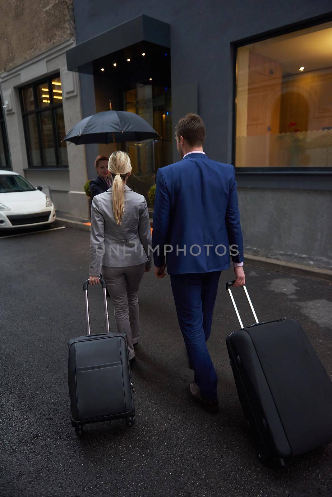 Young business people couple entering city  hotel, looking for room, holding suitcases while walking on street