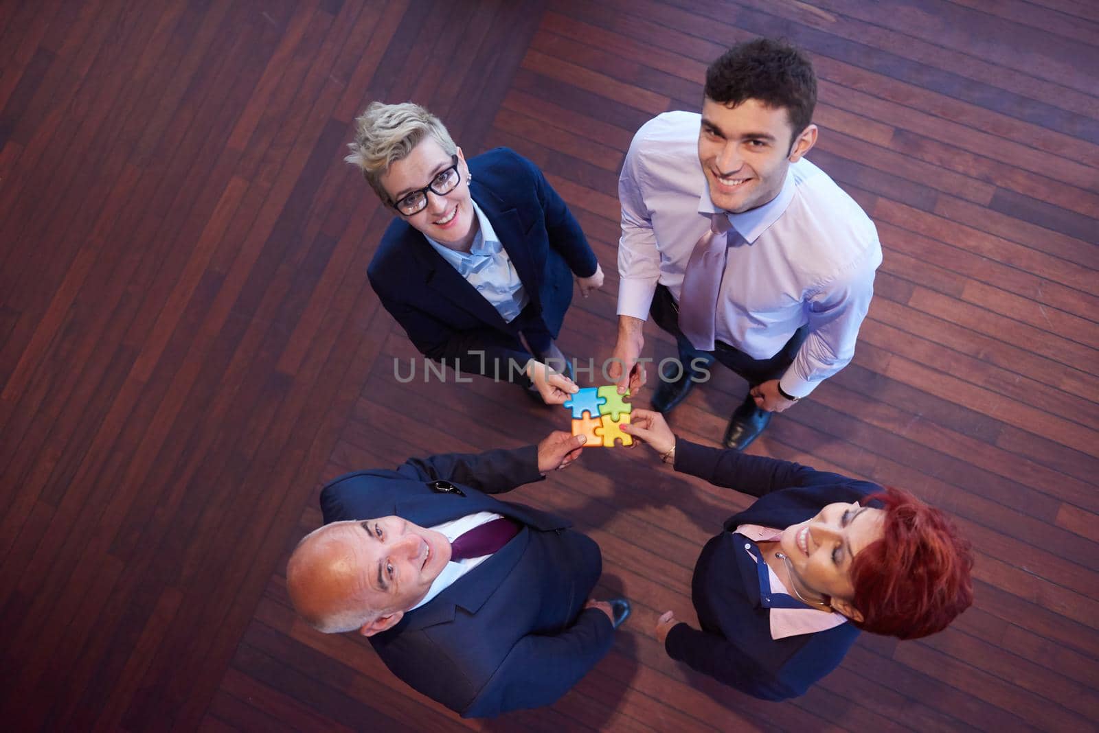 business people group assembling jigsaw puzzle and represent team support and help concept, top view perspective at modern bright office interior