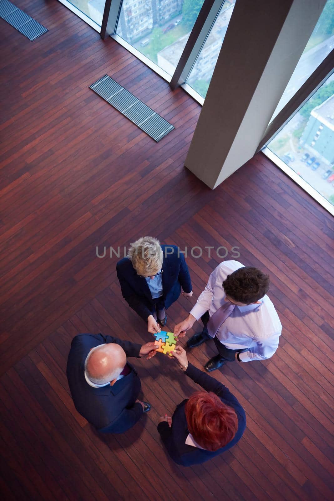 business people group assembling jigsaw puzzle and represent team support and help concept, top view perspective at modern bright office interior