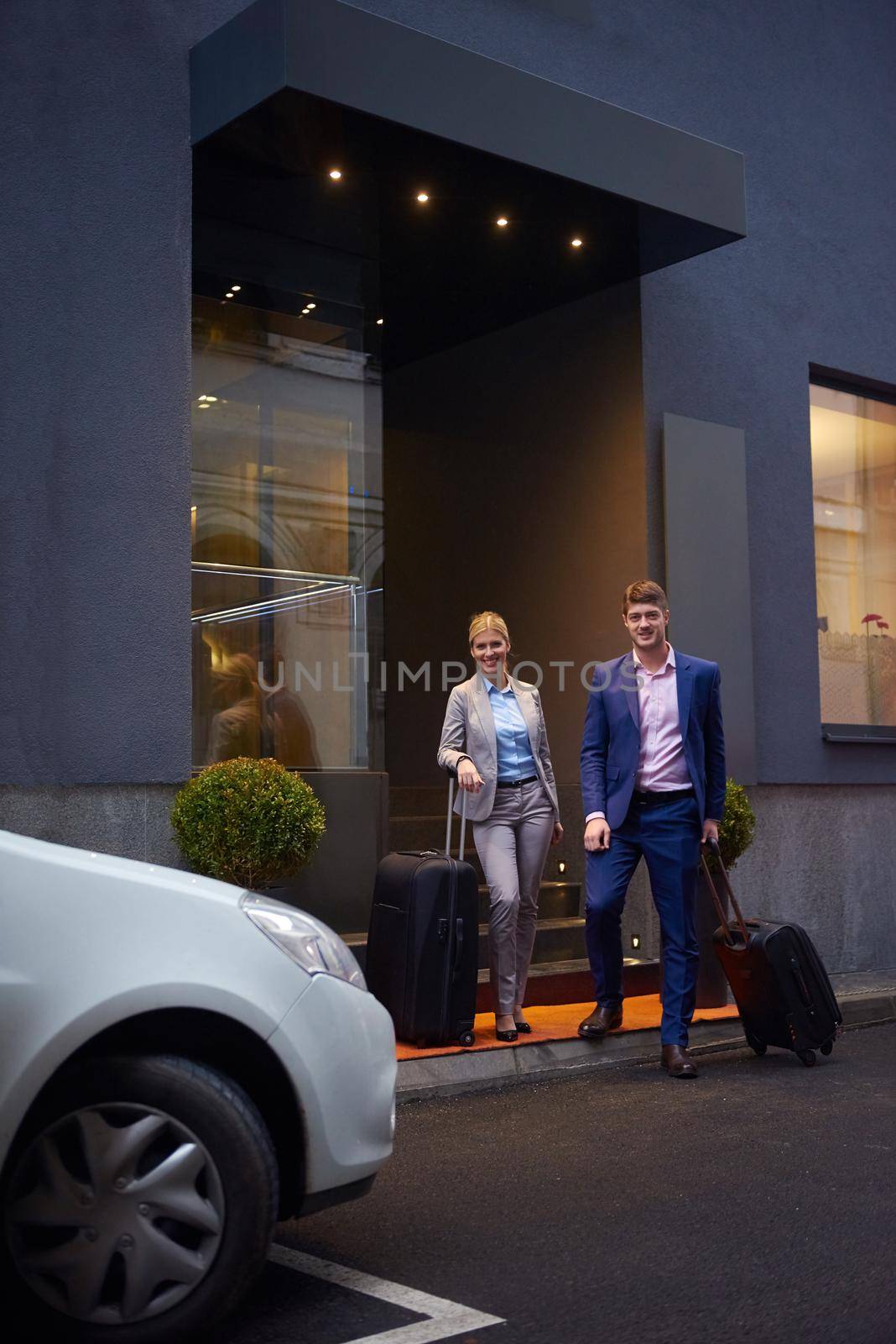 Young business people couple entering city  hotel, looking for room, holding suitcases while walking on street