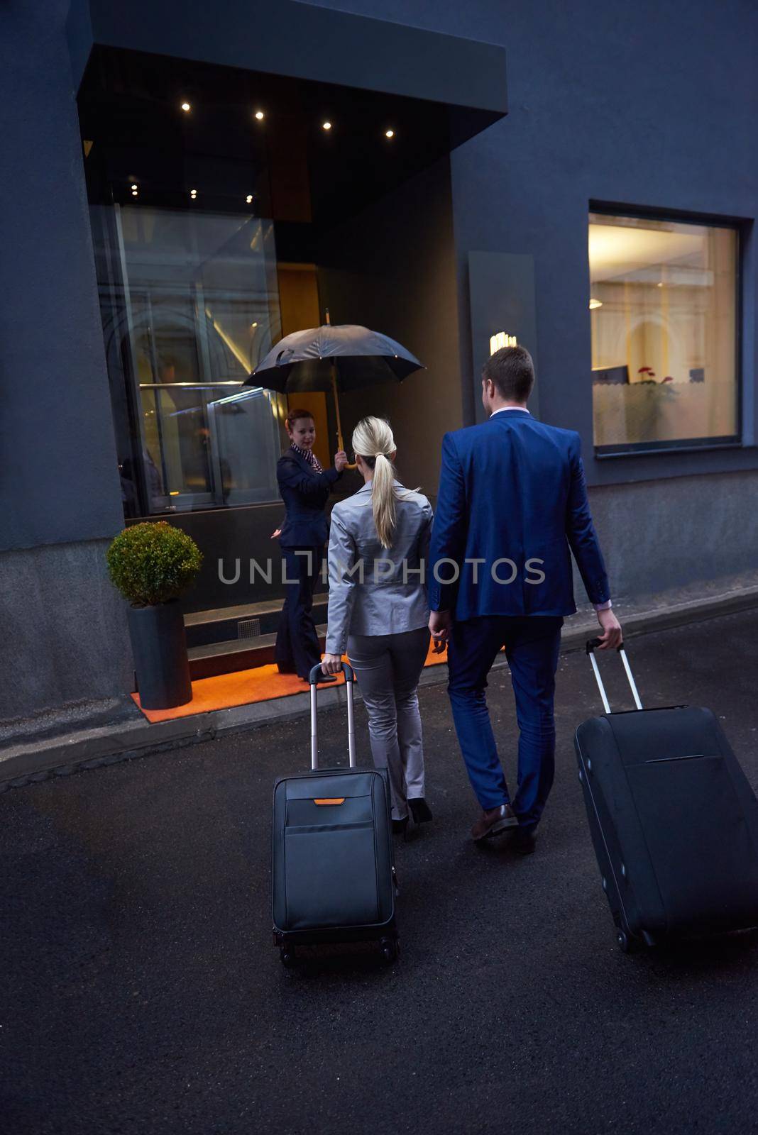 Young business people couple entering city  hotel, looking for room, holding suitcases while walking on street