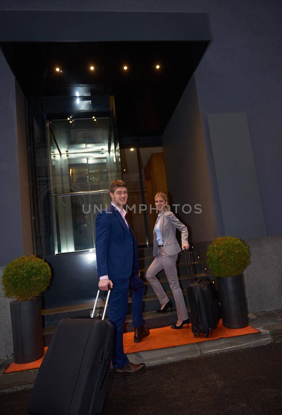 Young business people couple entering city  hotel, looking for room, holding suitcases while walking on street