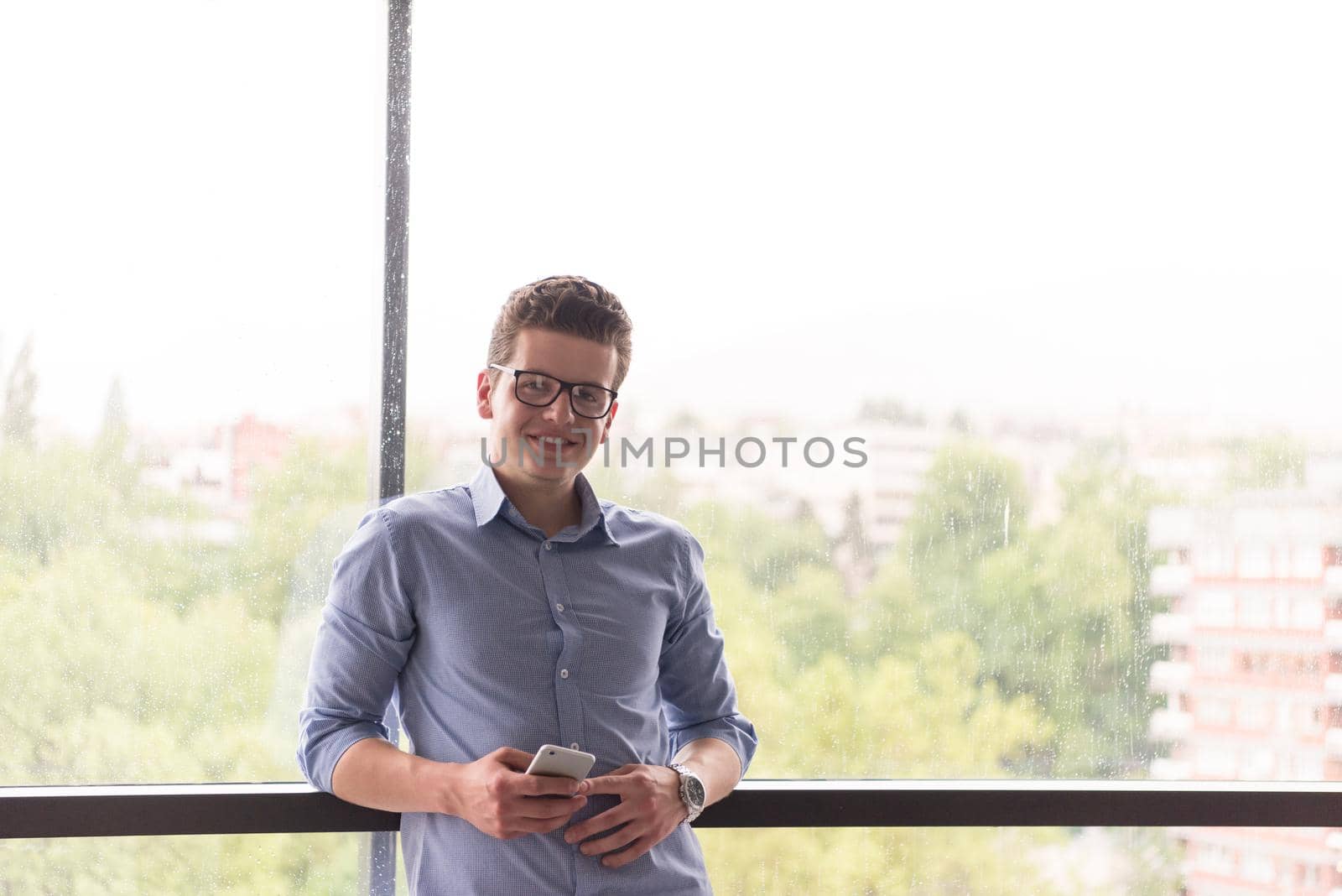businessman using a phone beside window of modern office
