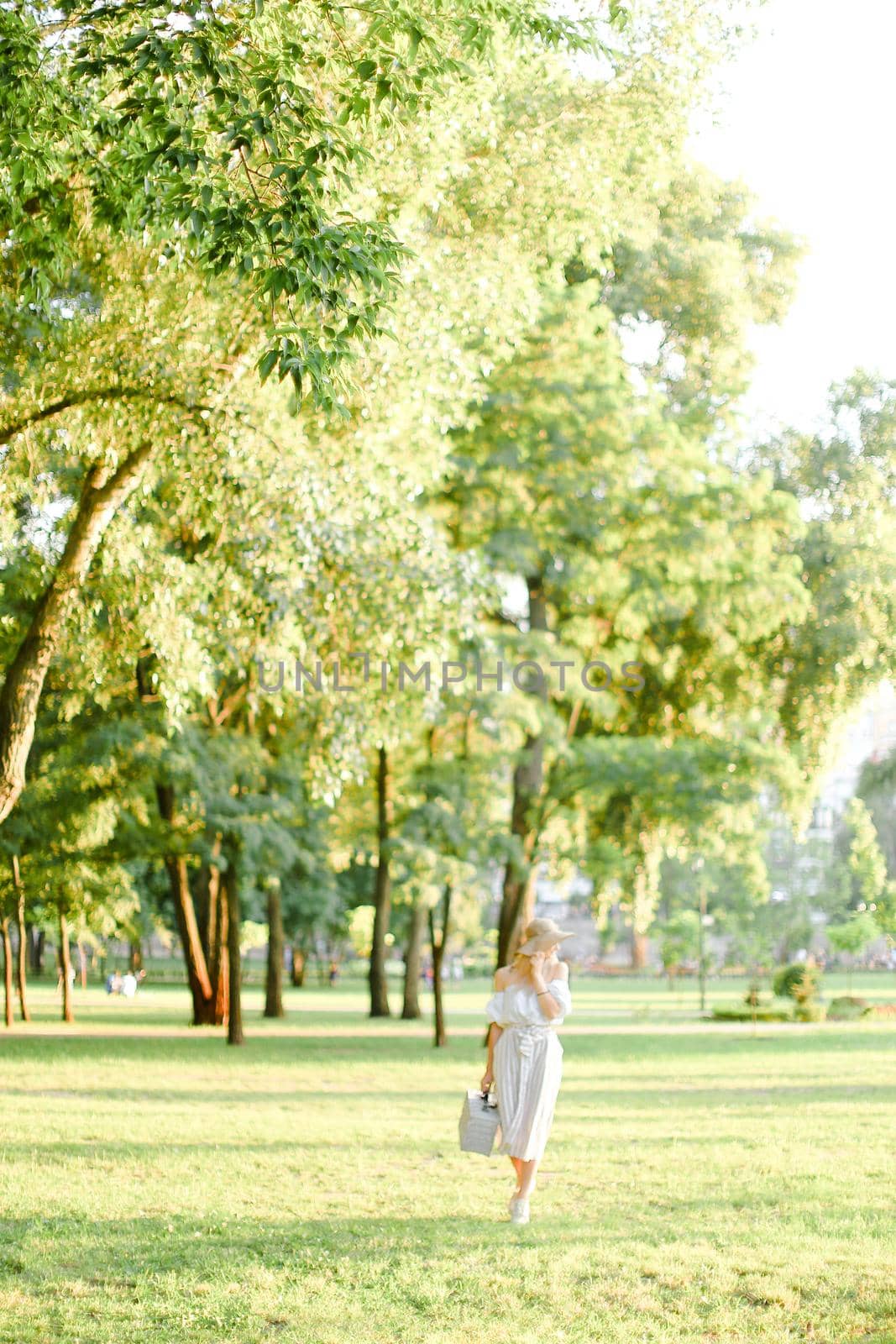 Young caucasian woman wearing hat walking in park with bag in sunny day. by sisterspro