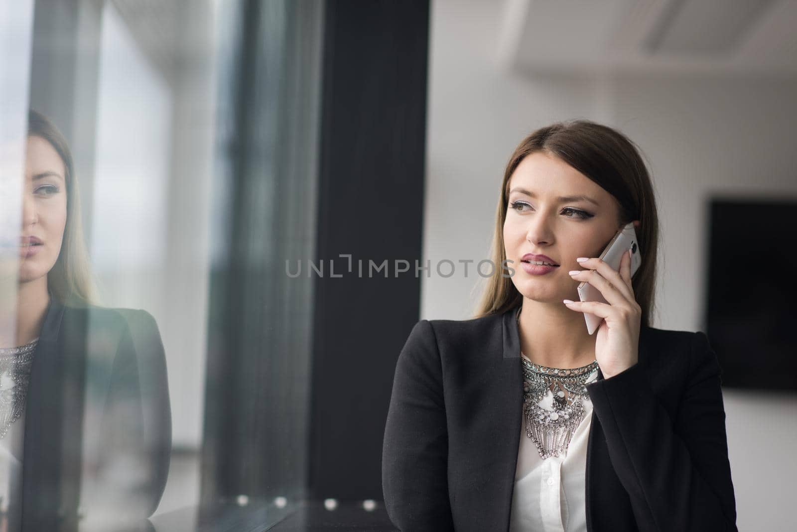 businesswoman speeking on phone beside window of modern office