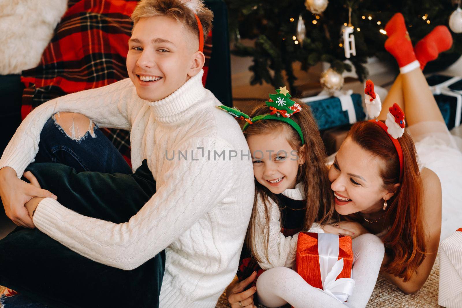 a happy family is lying on the floor of the house with New Year's gifts, next to the Christmas tree,