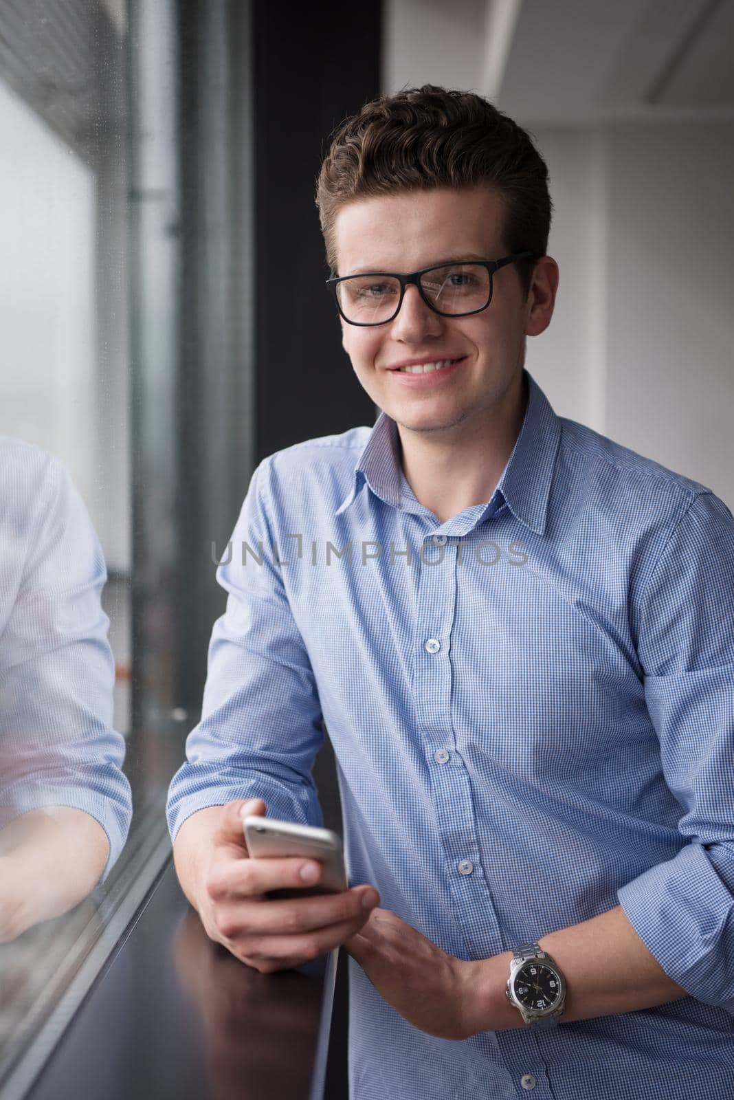 businessman using a phone beside window of modern office