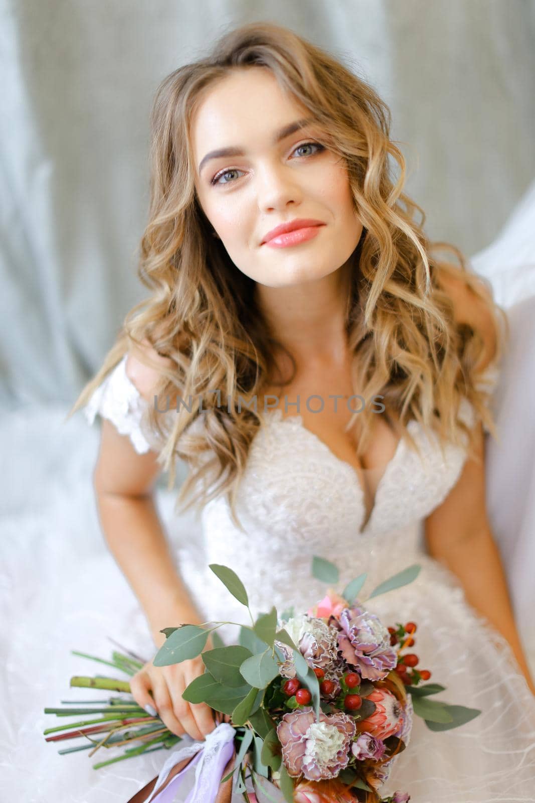 Blonde bride with bouquet of flowers sitting at studio. Concept of bridal make up, photo session and wedding.