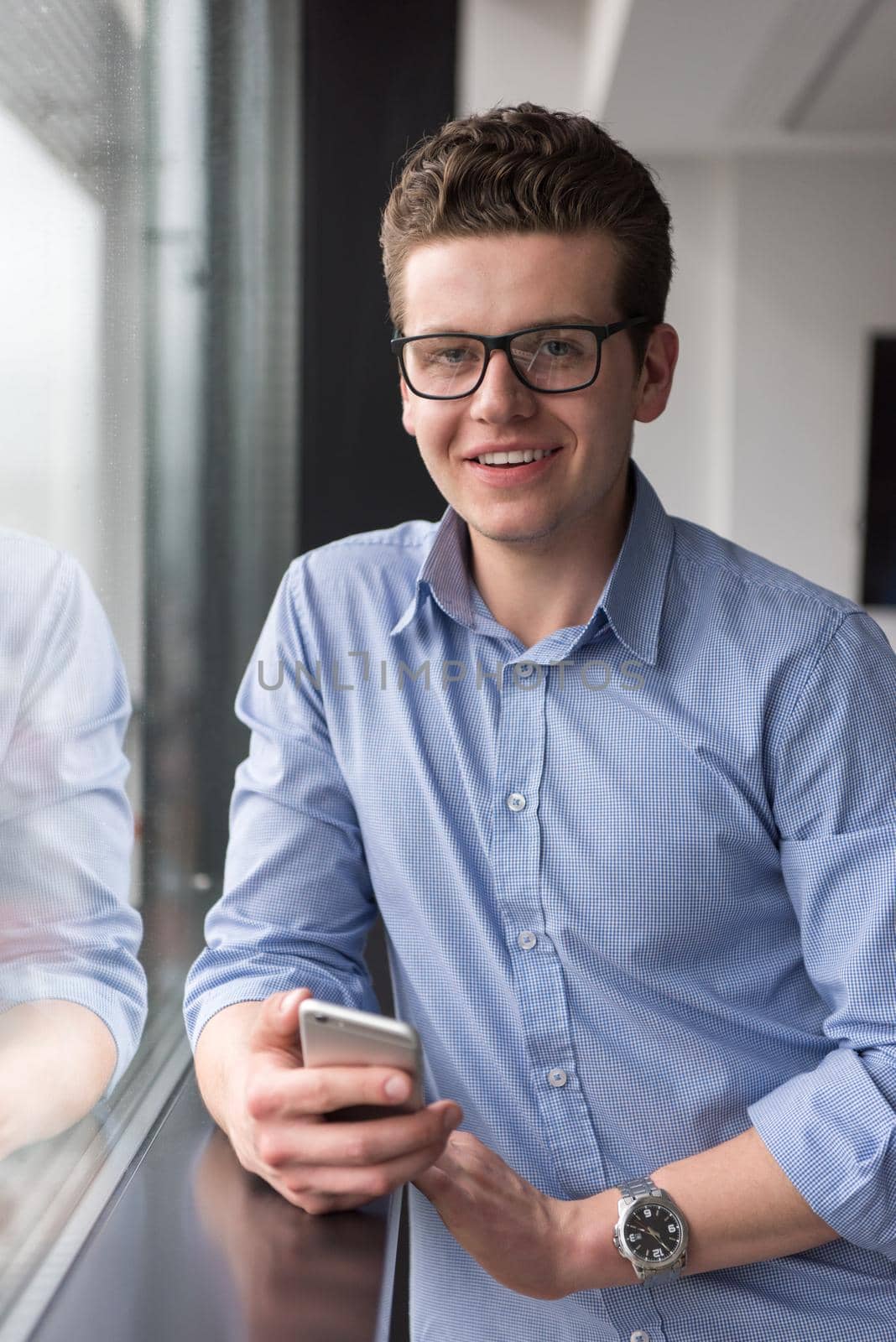 businessman using a phone beside window of modern office