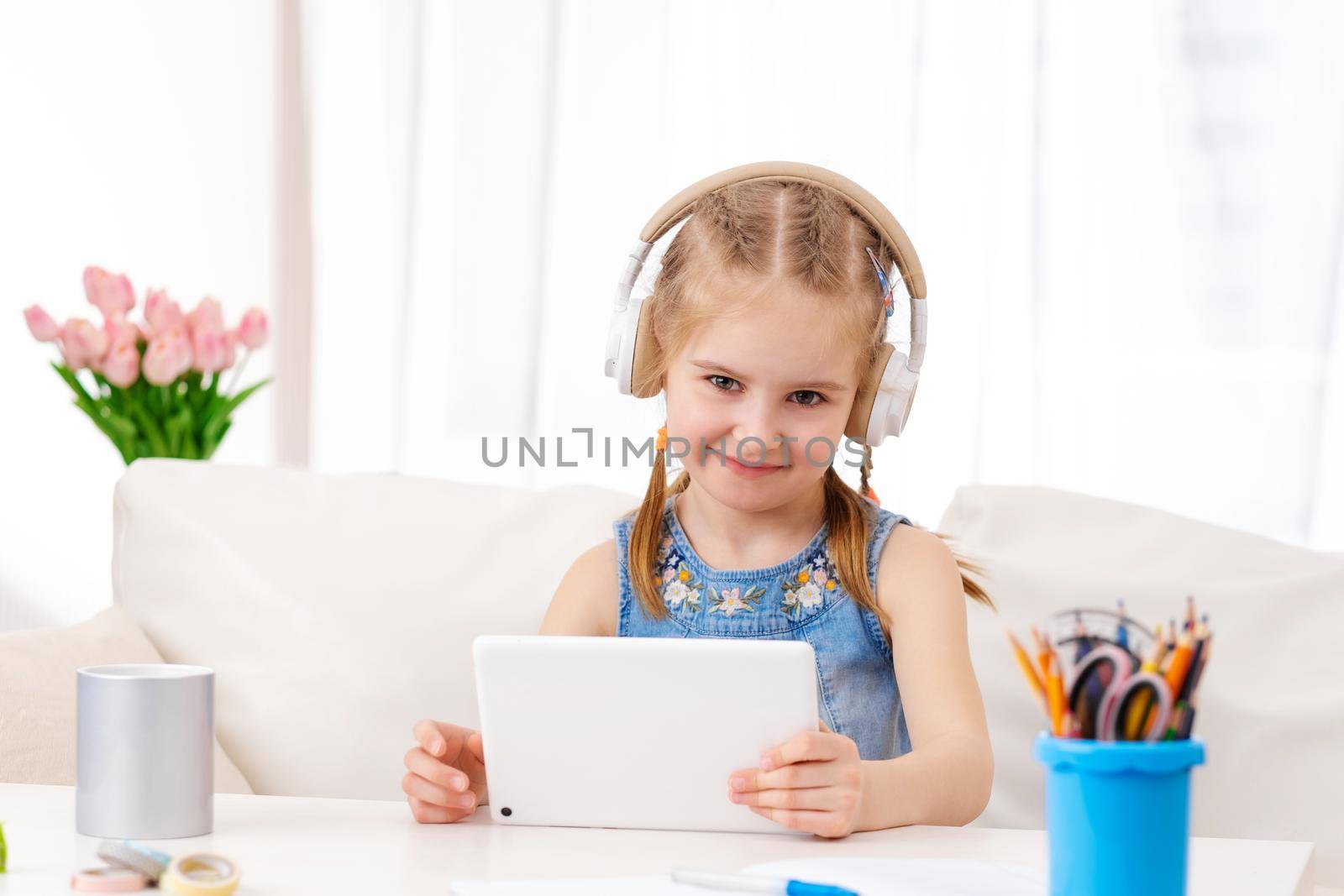 Beatiful little girl with white tablet with headphones on, in the room