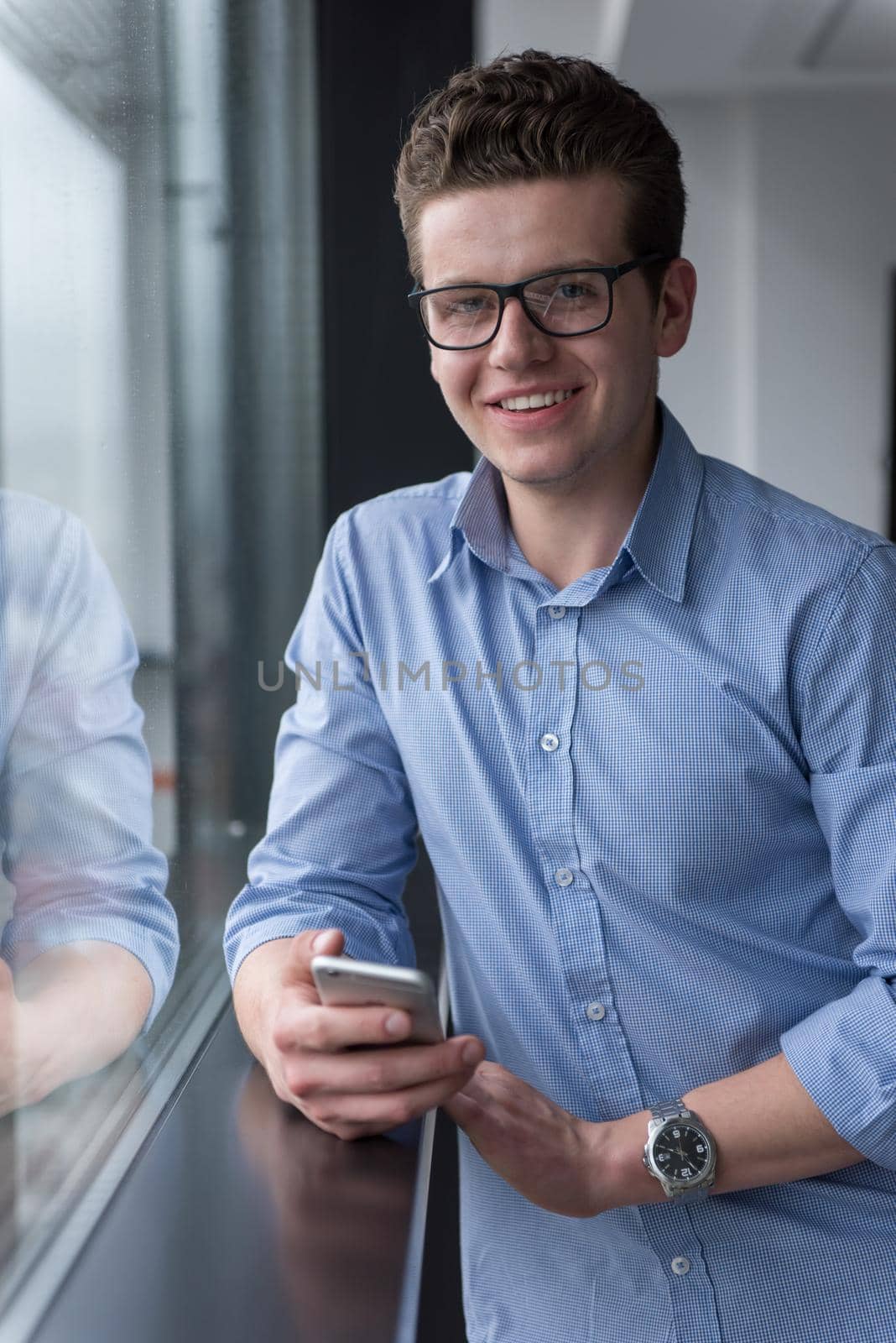 businessman using a phone beside window of modern office