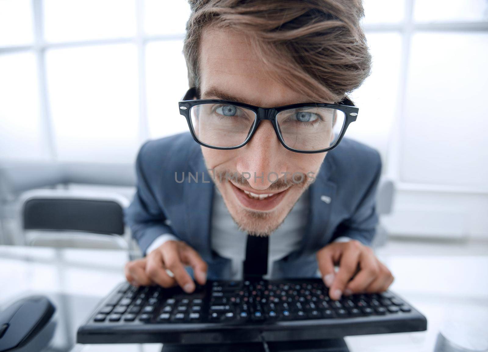 young businessman typing on computer keyboard with funny face expression isolated in the office