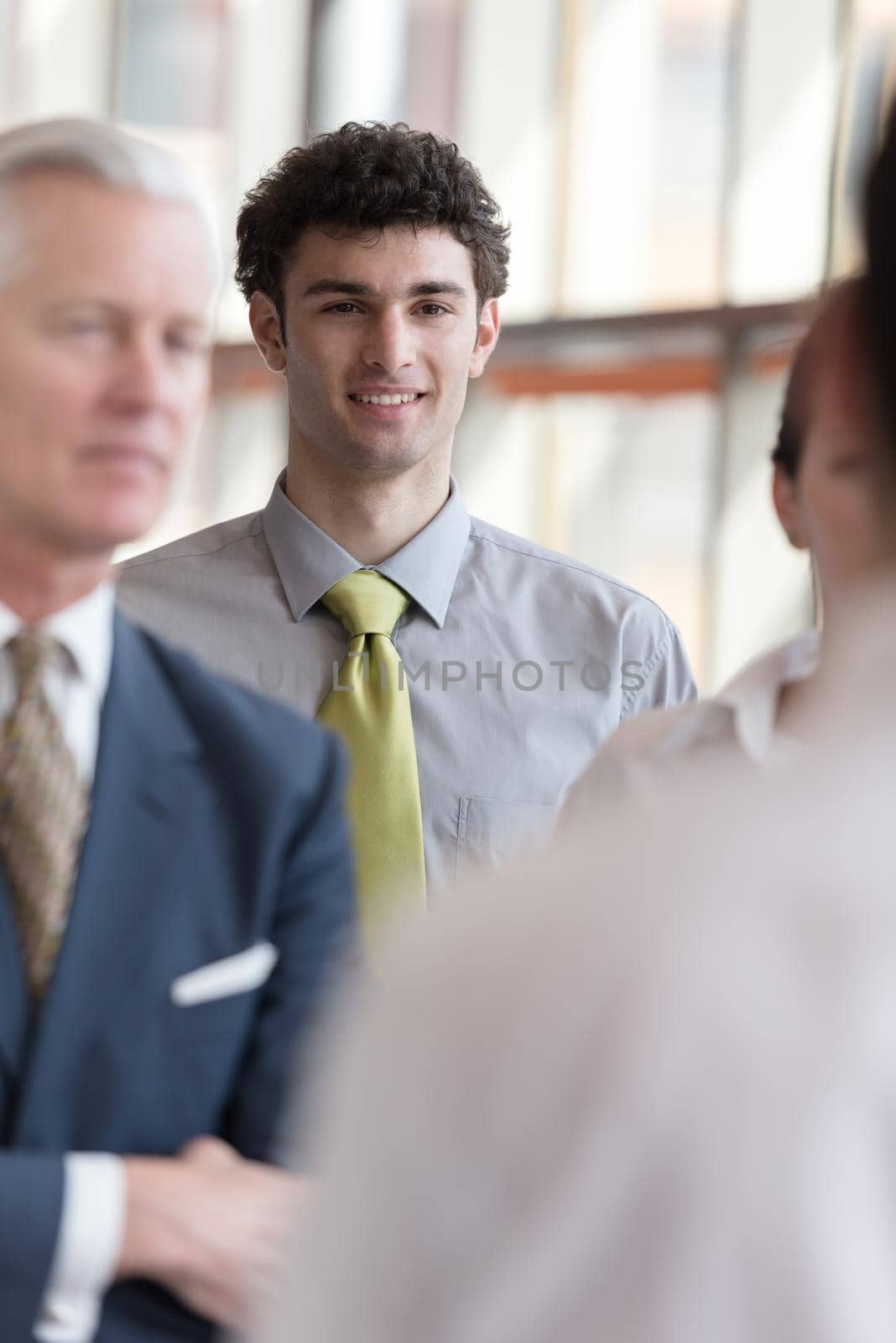 portrait of young business man with curly hair and  at modern bright office  interior with big windows in background and people group in front