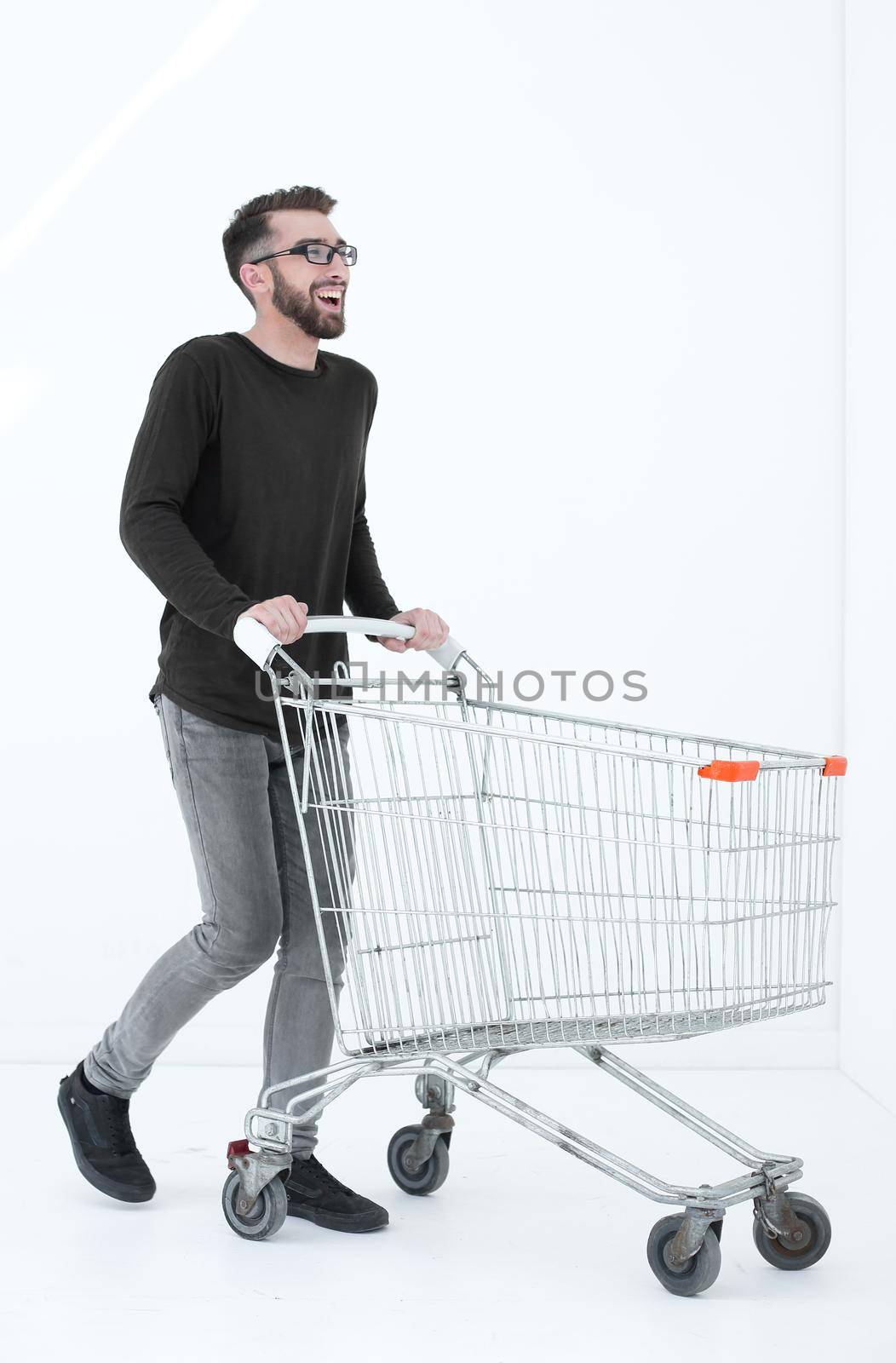Young man running and pushing an empty shopping cart isolated on white background