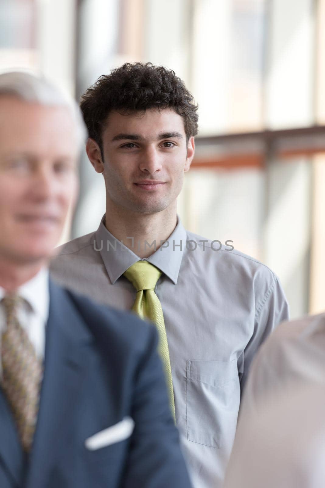 portrait of young business man with curly hair and  at modern bright office  interior with big windows in background and people group in front