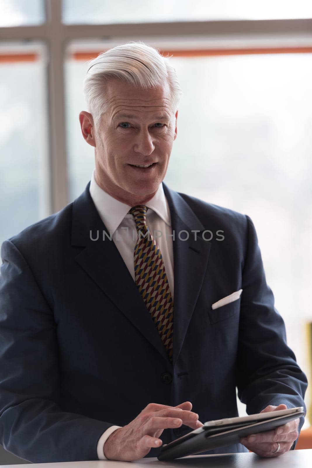 handsome senior business man with grey hair working on tablet computer at modern bright office interior