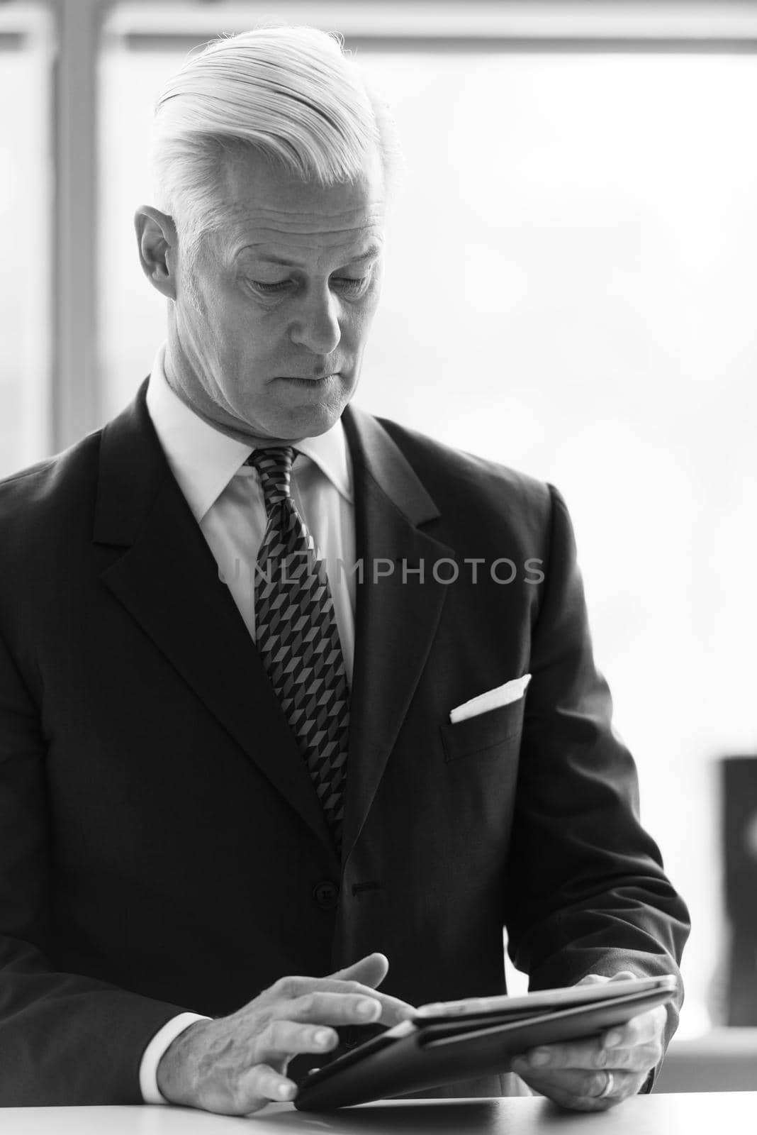 handsome senior business man with grey hair working on tablet computer at modern bright office interior