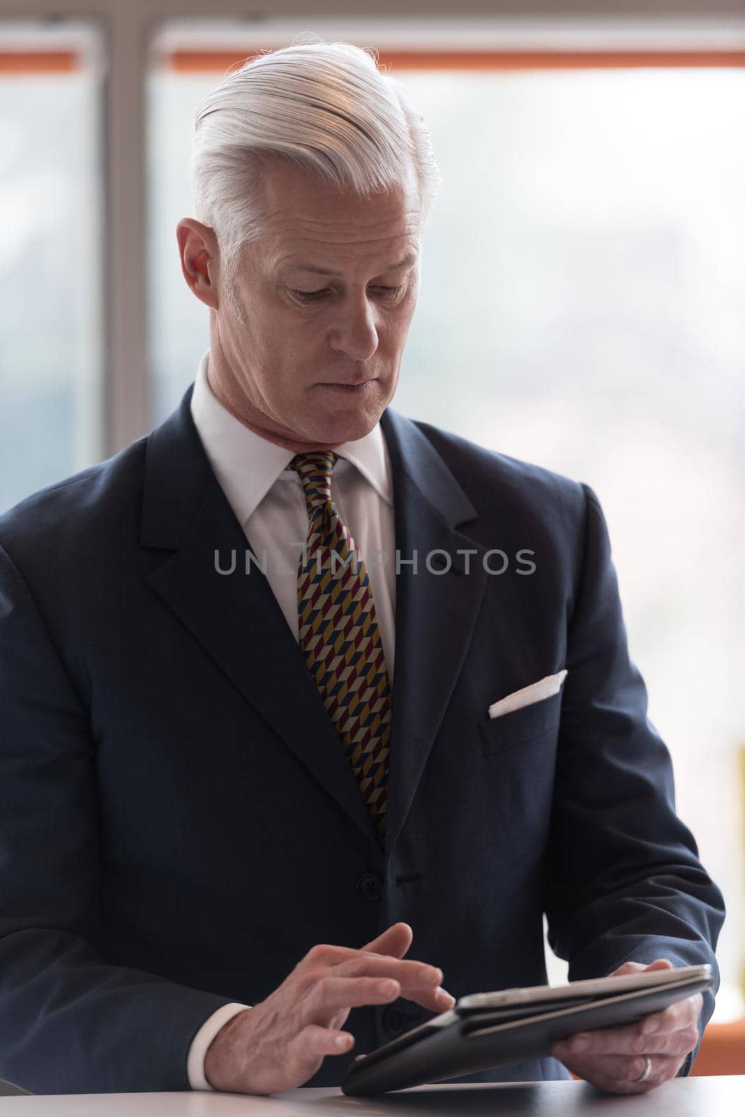 handsome senior business man with grey hair working on tablet computer at modern bright office interior