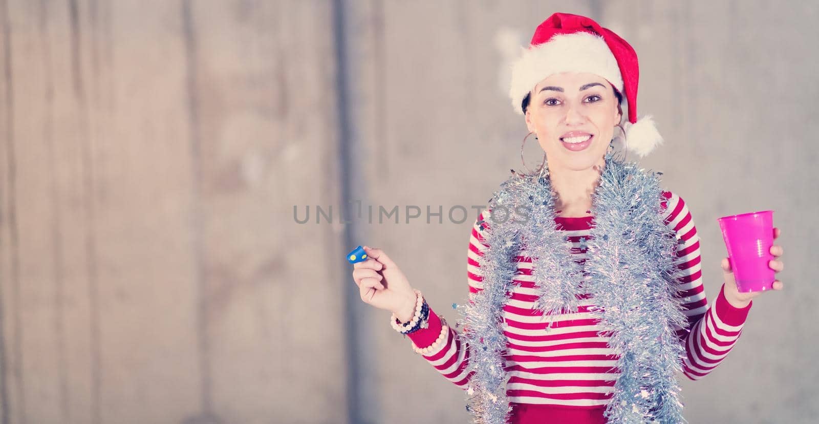 young happy casual business woman wearing a red hat and blowing party whistle while dancing during new years party in front of concrete wall