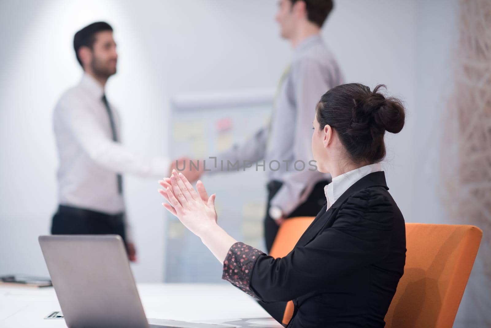 young business woman on meeting usineg laptop computer, blured group of people in background at  modern bright startup office interior taking notes on white flip board and brainstorming about plans and ideas