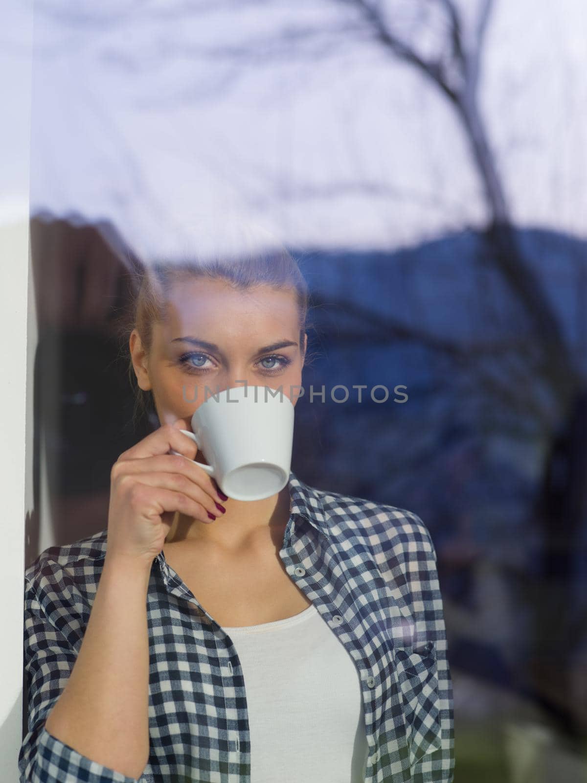 young woman drinking morning coffee by the window by dotshock