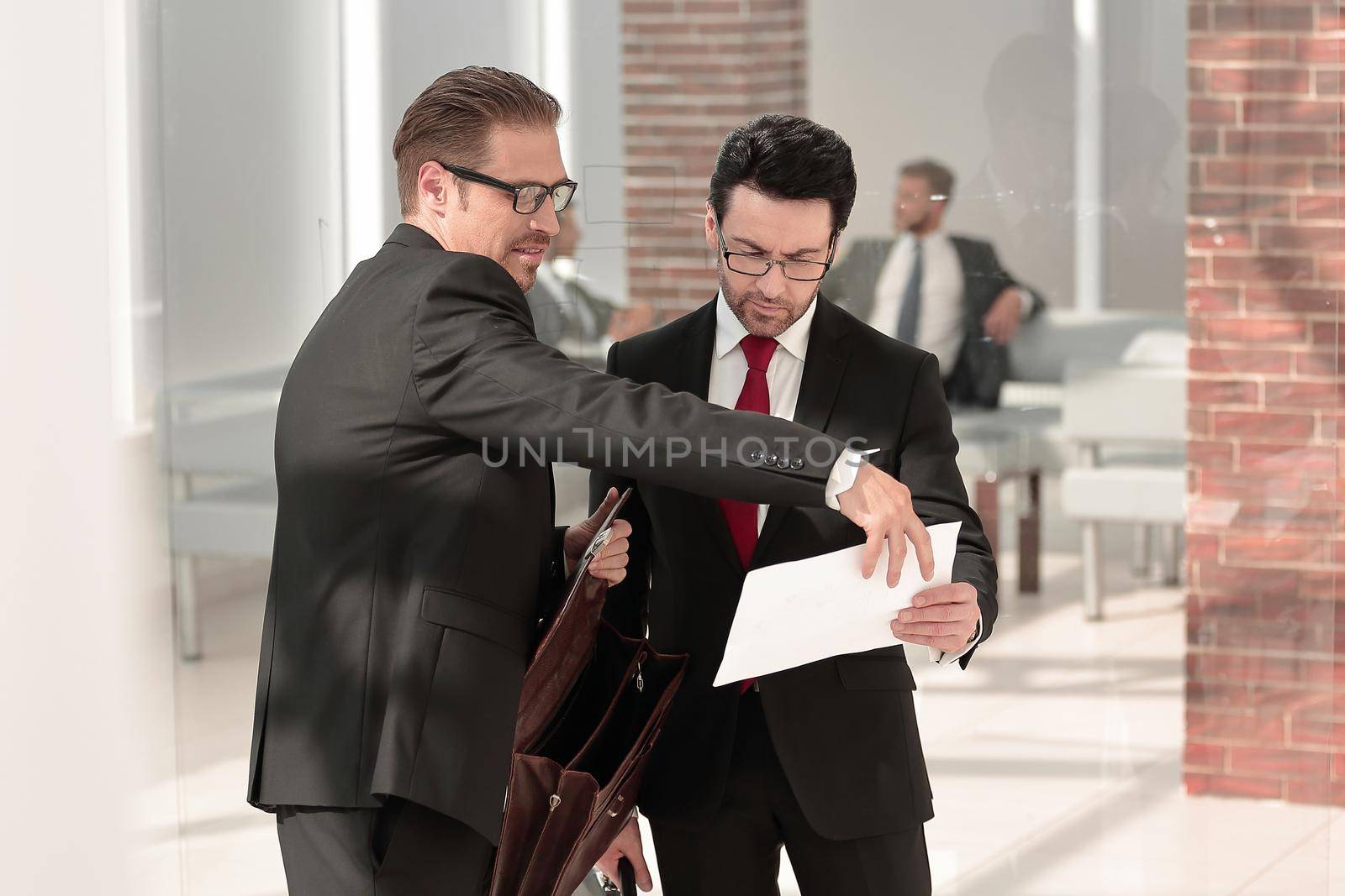 Two focused colleagues stand in a modern office and deeply discuss documents
