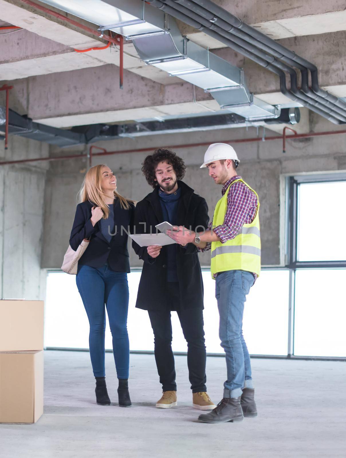 architect using tablet computer while showing house design plans to a young couple at construction site