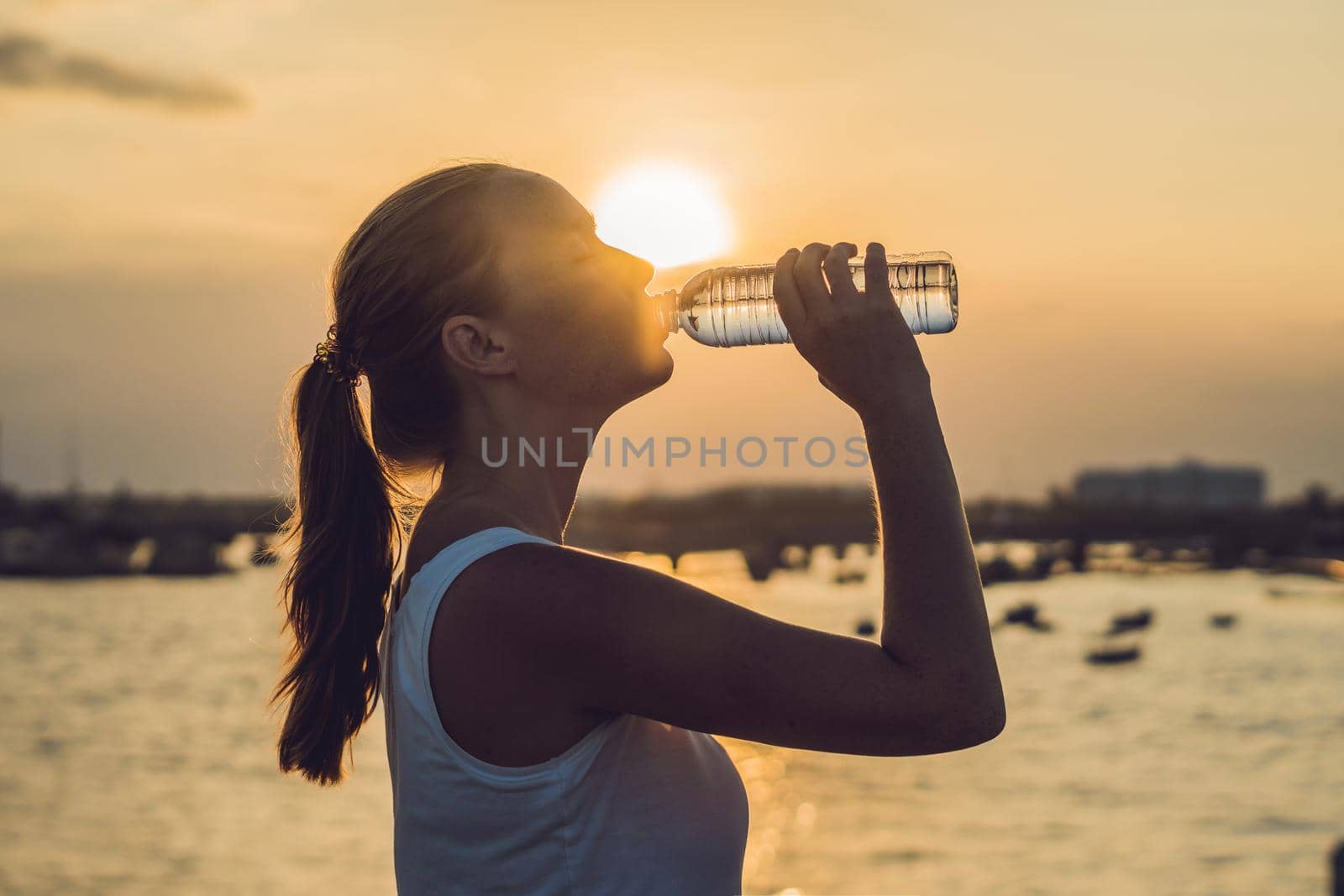 Sporty woman drinking water outdoor on sunny day by galitskaya