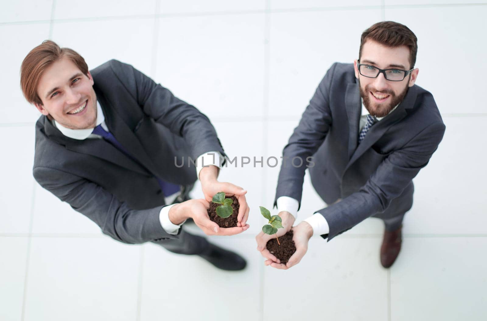 top view.two smiling businessmen with green sprout are looking at the camera