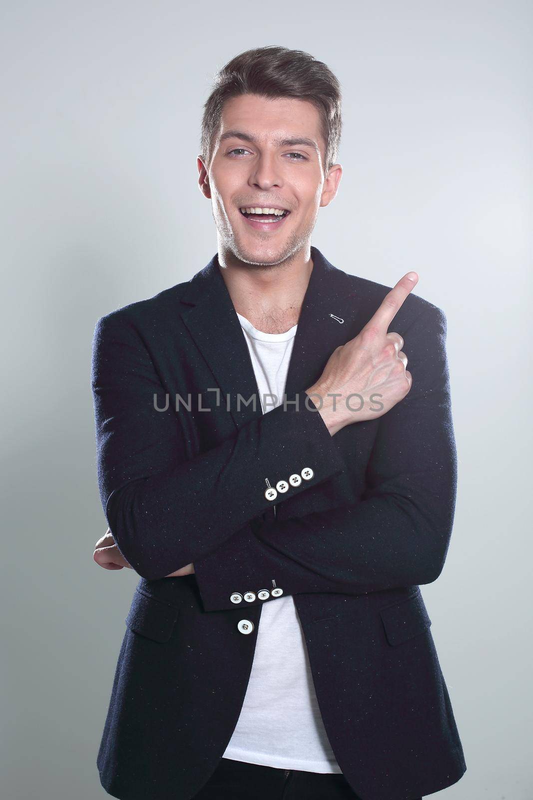 Close up portrait of young successful brunete stock-market broker guy on the gray background, he is smiling and is pointing on a copyspace with his finger