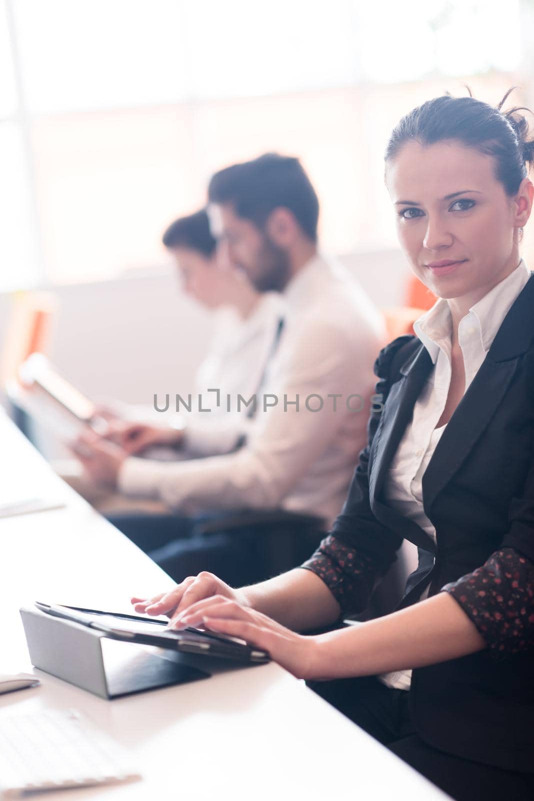 business woman on meeting usineg tablet computer, blured group of people in background at  modern bright startup office interior