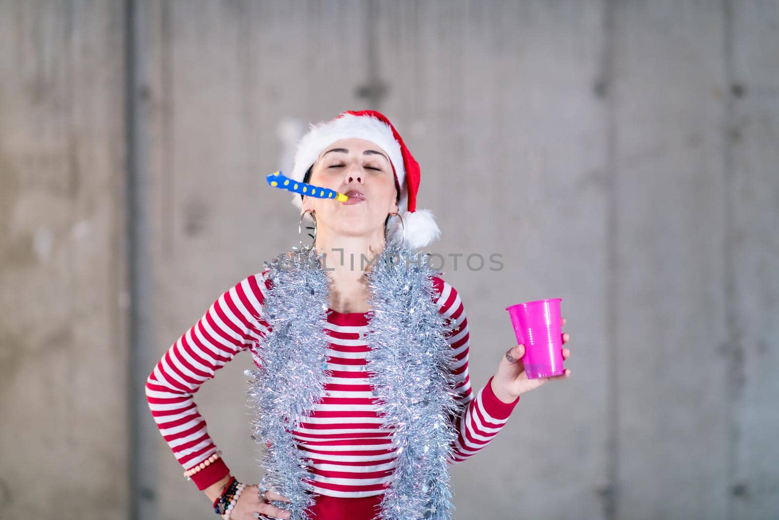 young happy casual business woman wearing a red hat and blowing party whistle while dancing during new years party in front of concrete wall