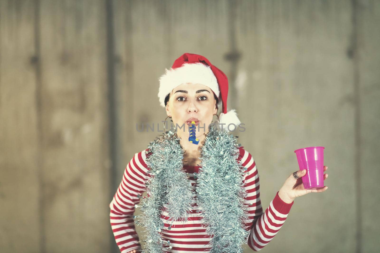 young happy casual business woman wearing a red hat and blowing party whistle while dancing during new years party in front of concrete wall