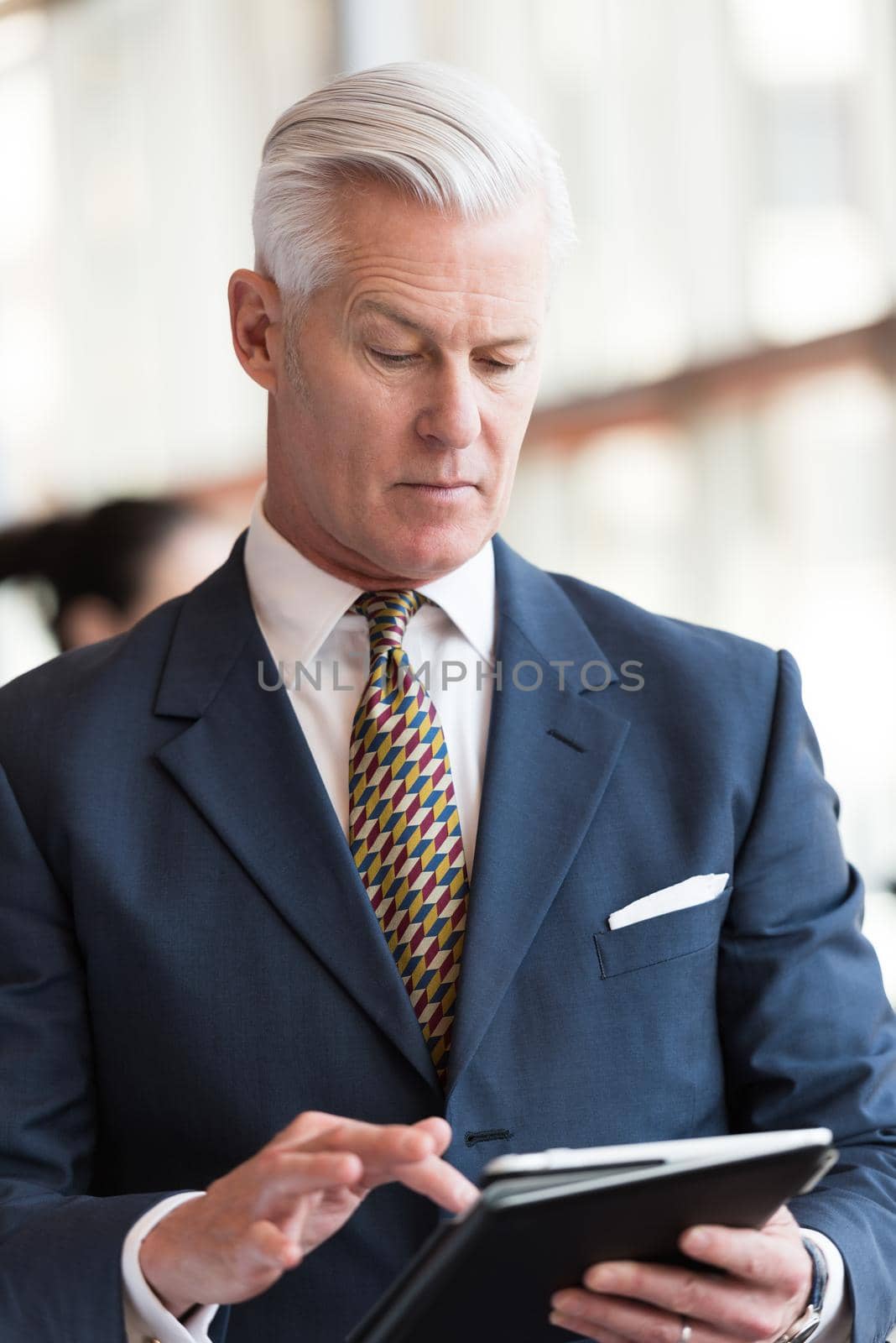 handsome senior business man with grey hair working on tablet computer at modern bright office interior