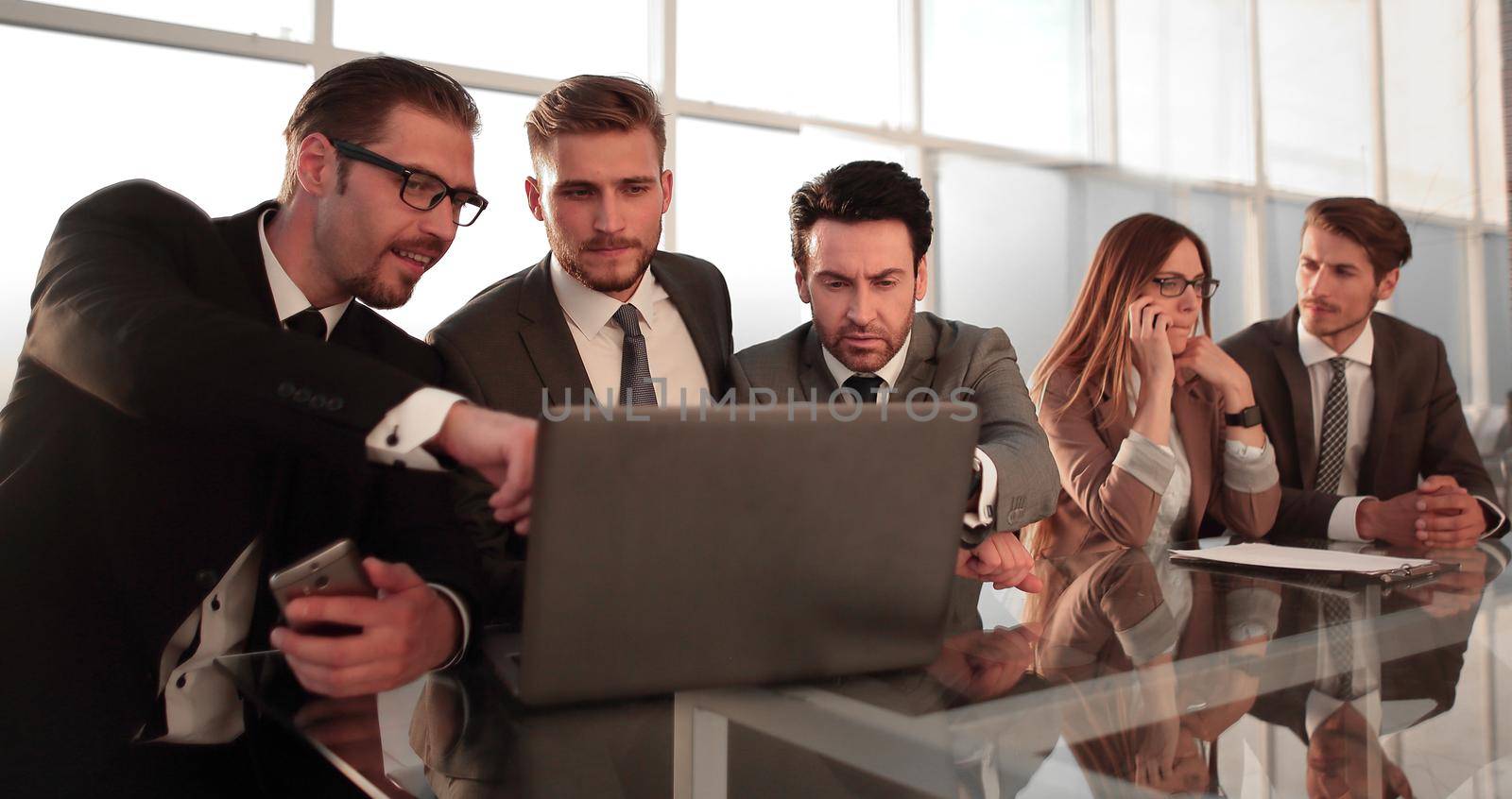Businessmen and businessmen using laptop together, sitting in front of windows of office building