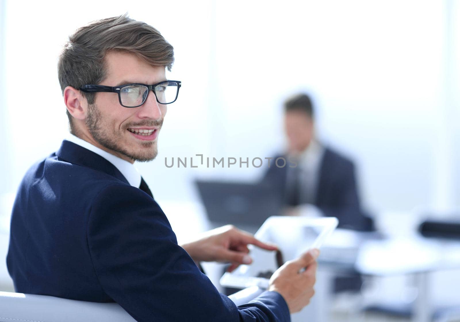 young man with glasses looks at camera and smiles using tablet