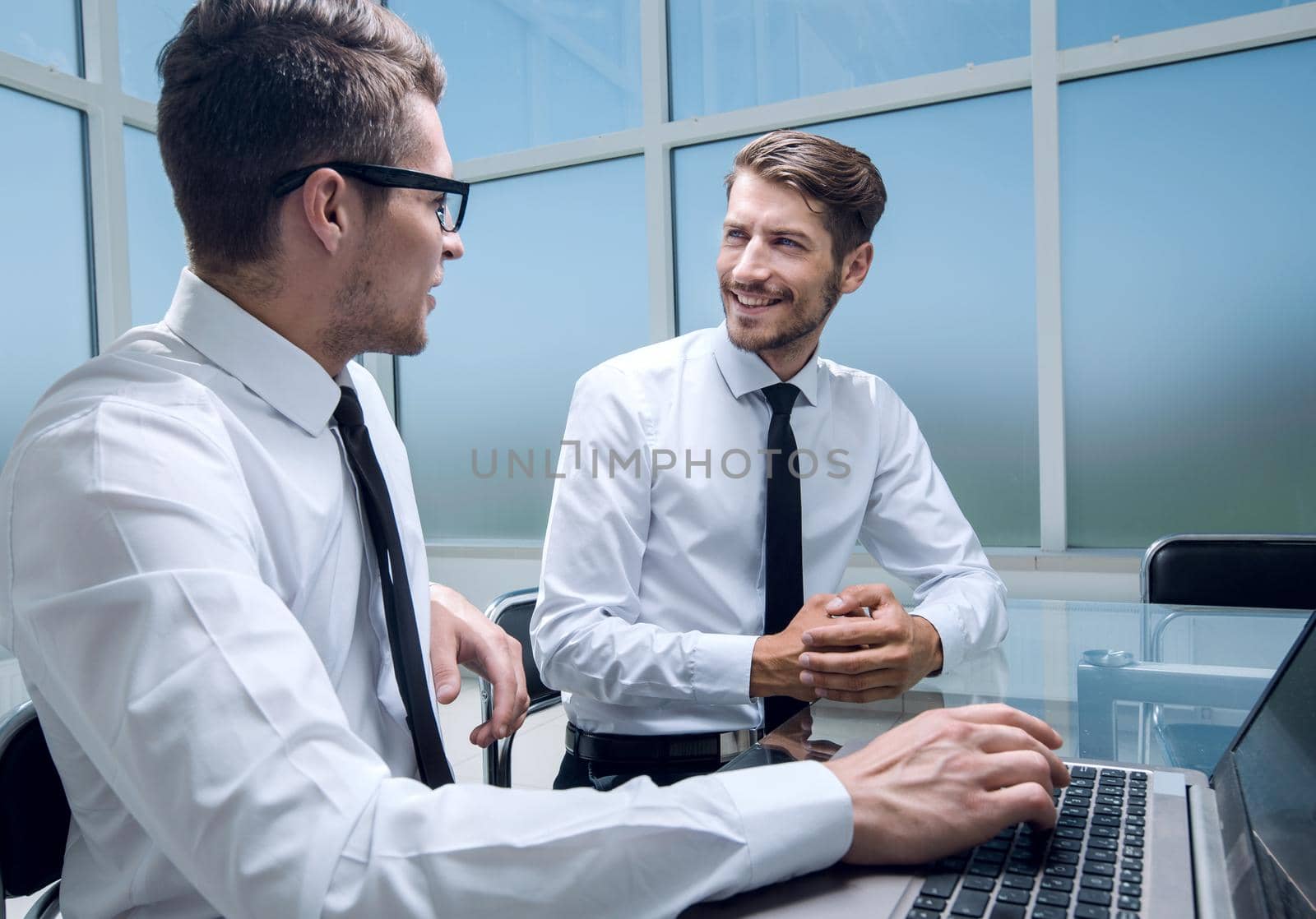 young colleagues sit at the desk in the office and work on laptops