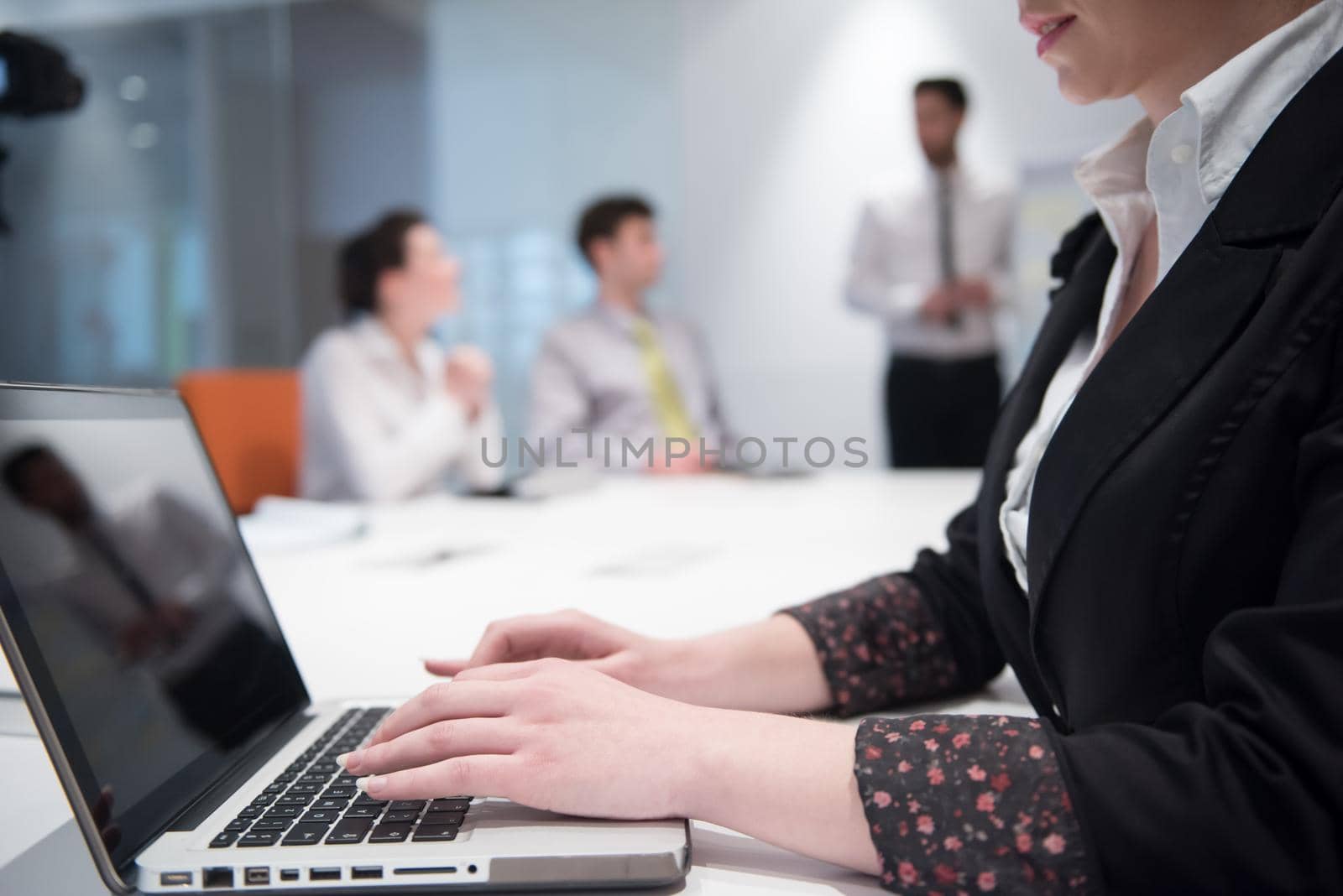 young business woman on meeting usineg laptop computer, blured group of people in background at  modern bright startup office interior taking notes on white flip board and brainstorming about plans and ideas