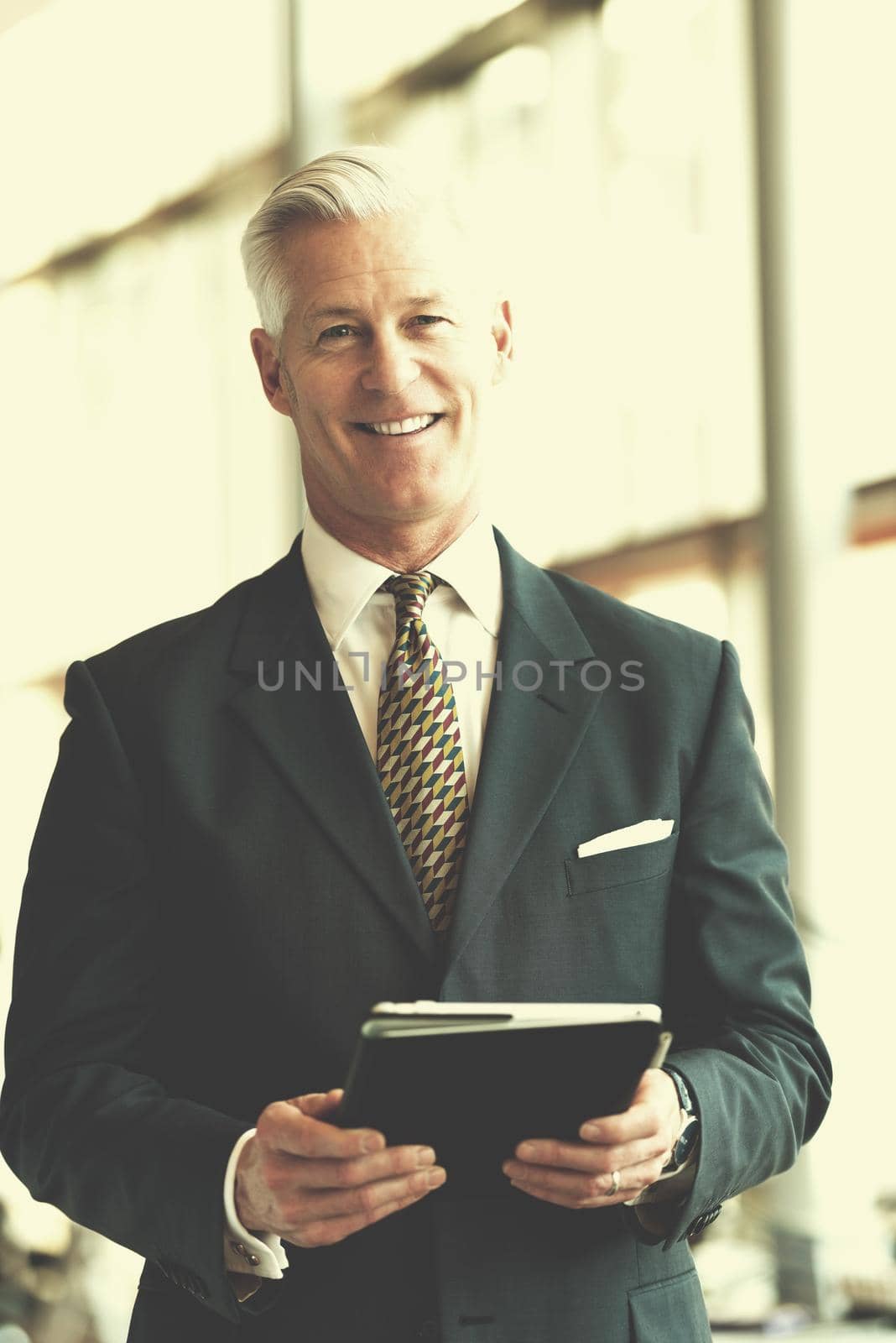 handsome senior business man with grey hair working on tablet computer at modern bright office interior