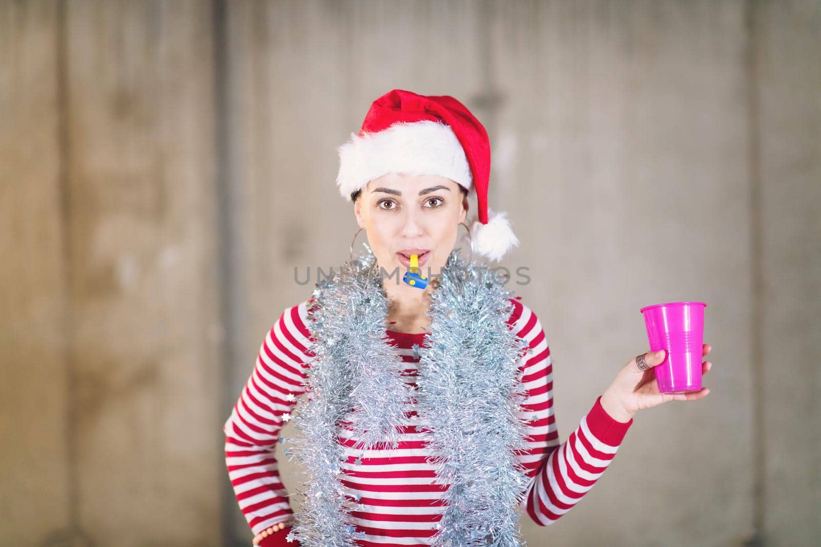 young happy casual business woman wearing a red hat and blowing party whistle while dancing during new years party in front of concrete wall