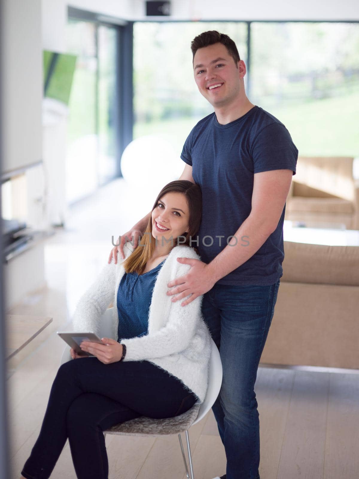 Young couple using tablet computer at luxury home together, looking at screen, smiling.