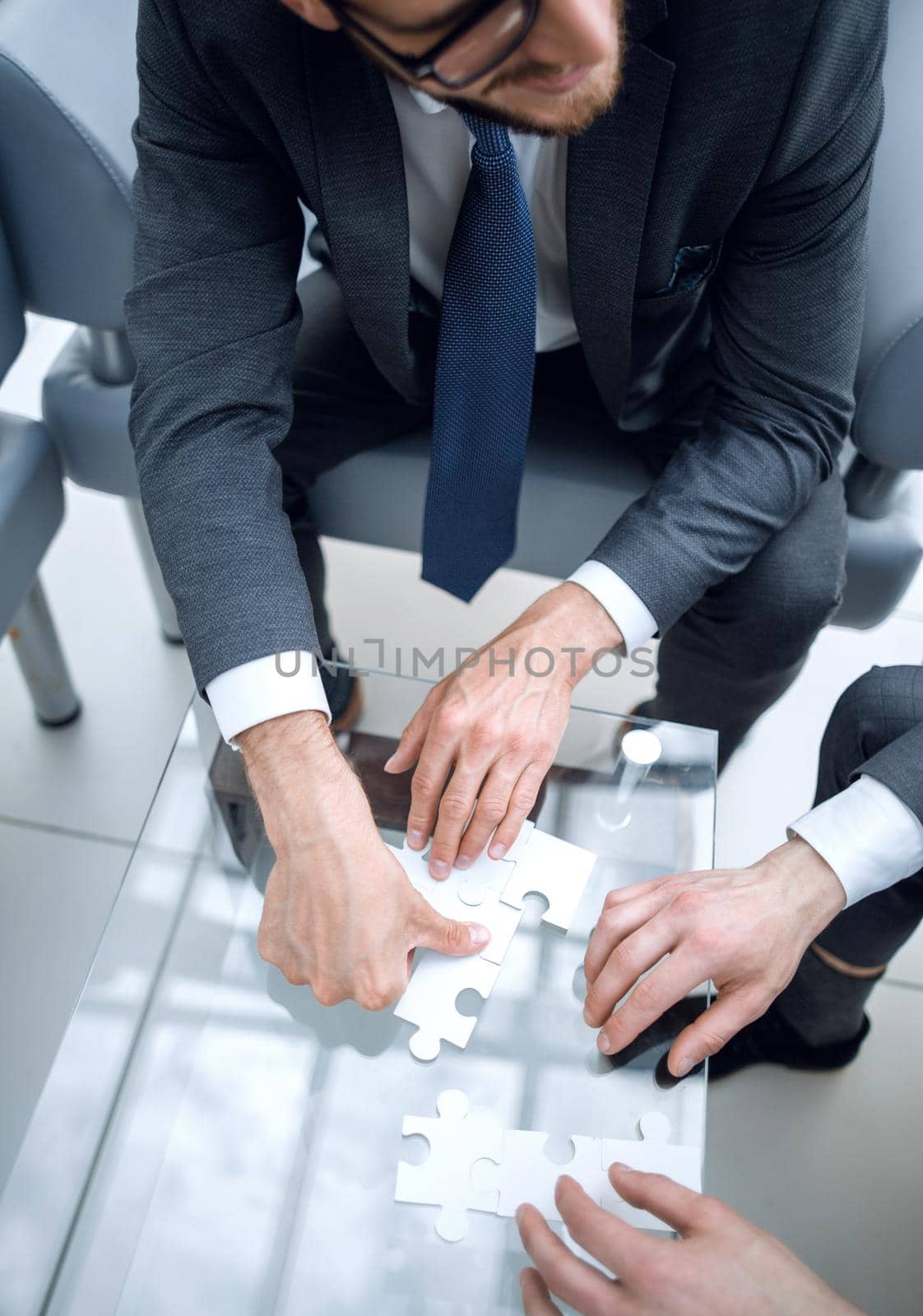 close up.business colleagues putting together a puzzle ,sitting at office Desk.the concept of cooperation