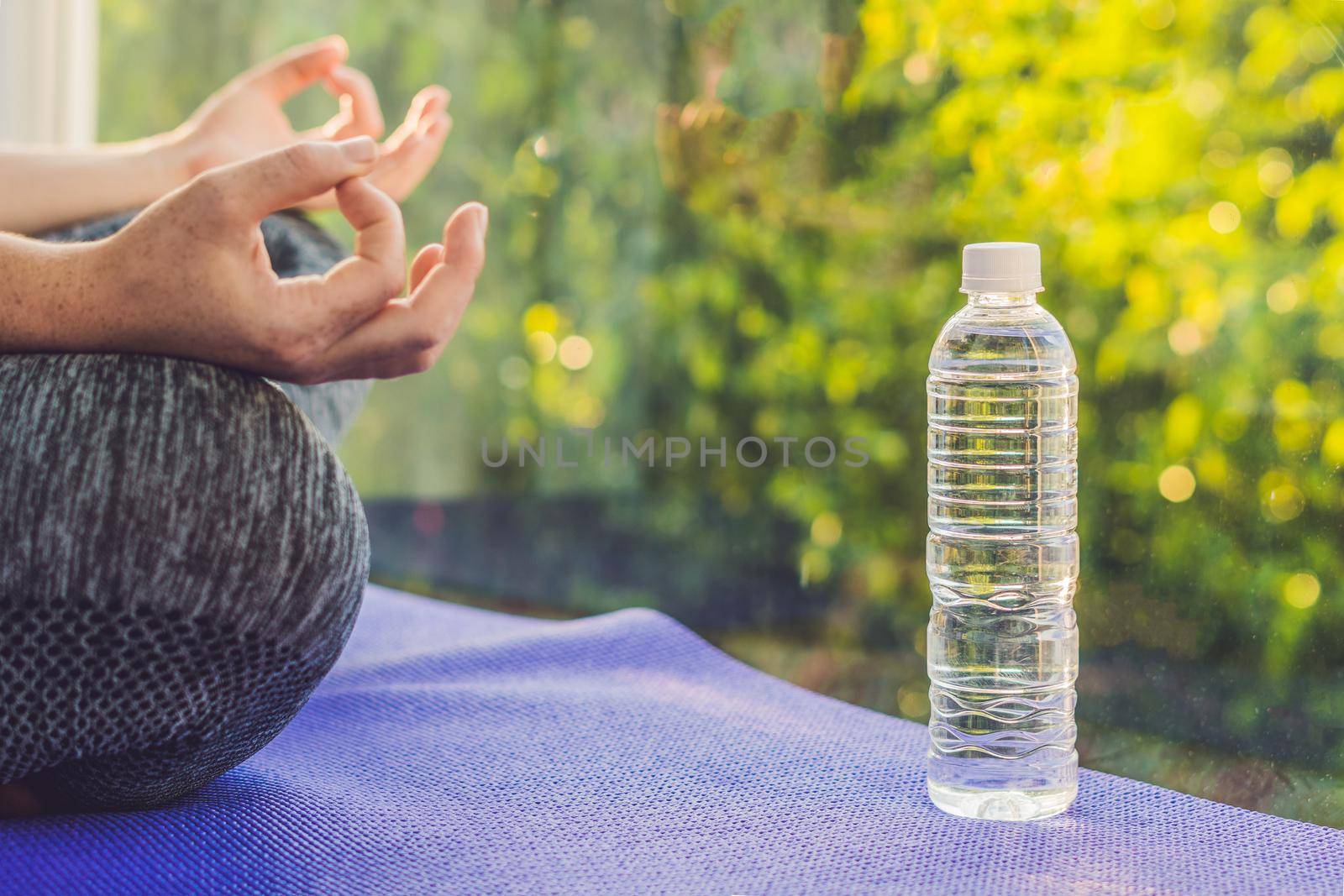 hand of a woman meditating in a yoga pose on a rug for yoga and a bottle of water.