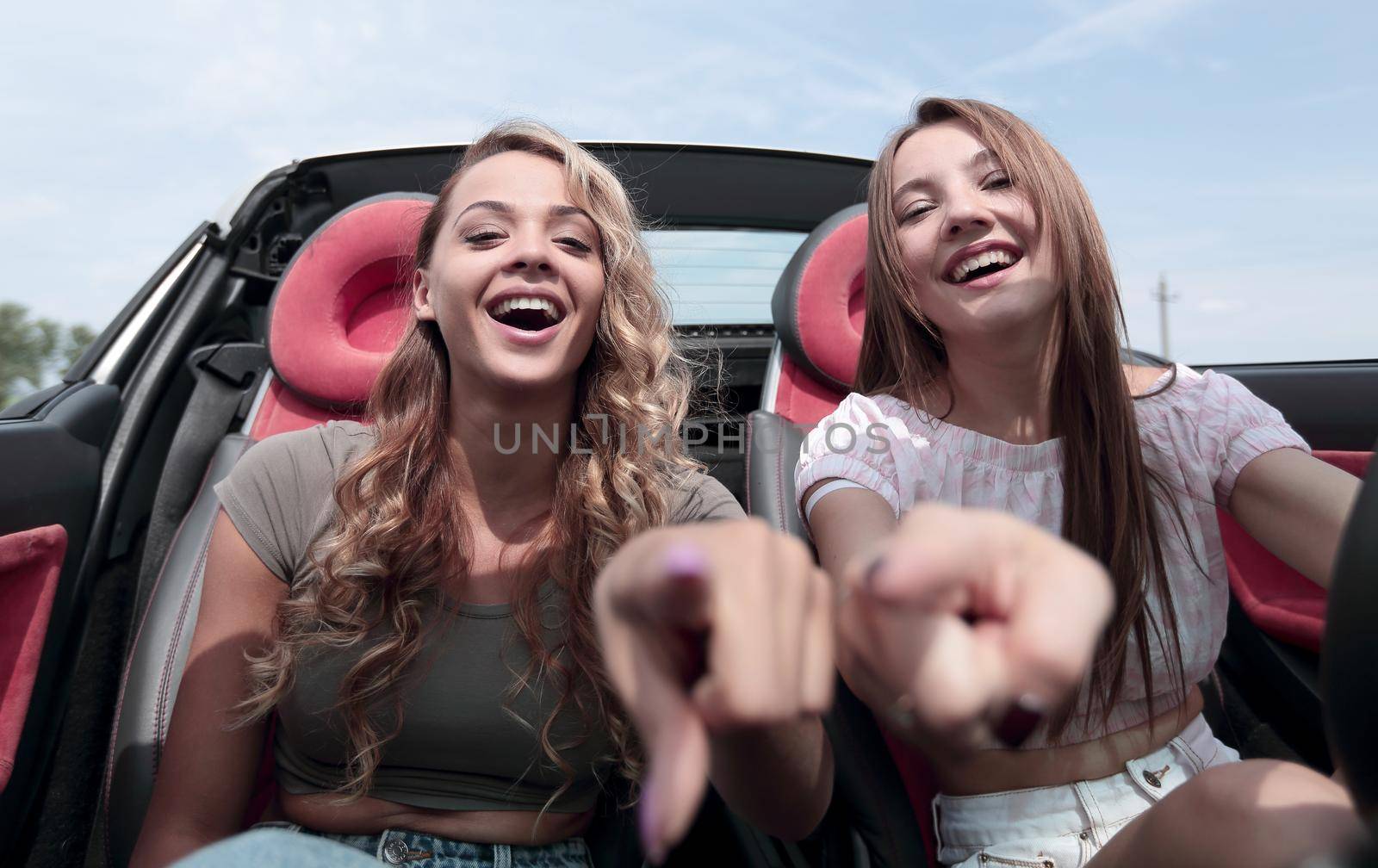 two happy girls sitting in the car and pointing at you.the concept of choice