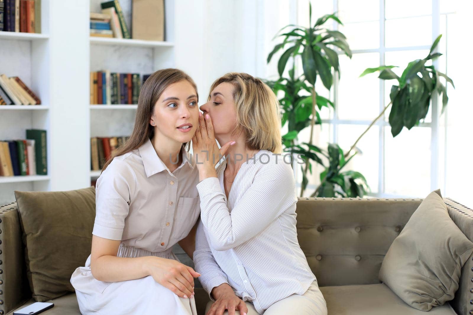 Happy middle aged mother and daughter talking on sofa in living room